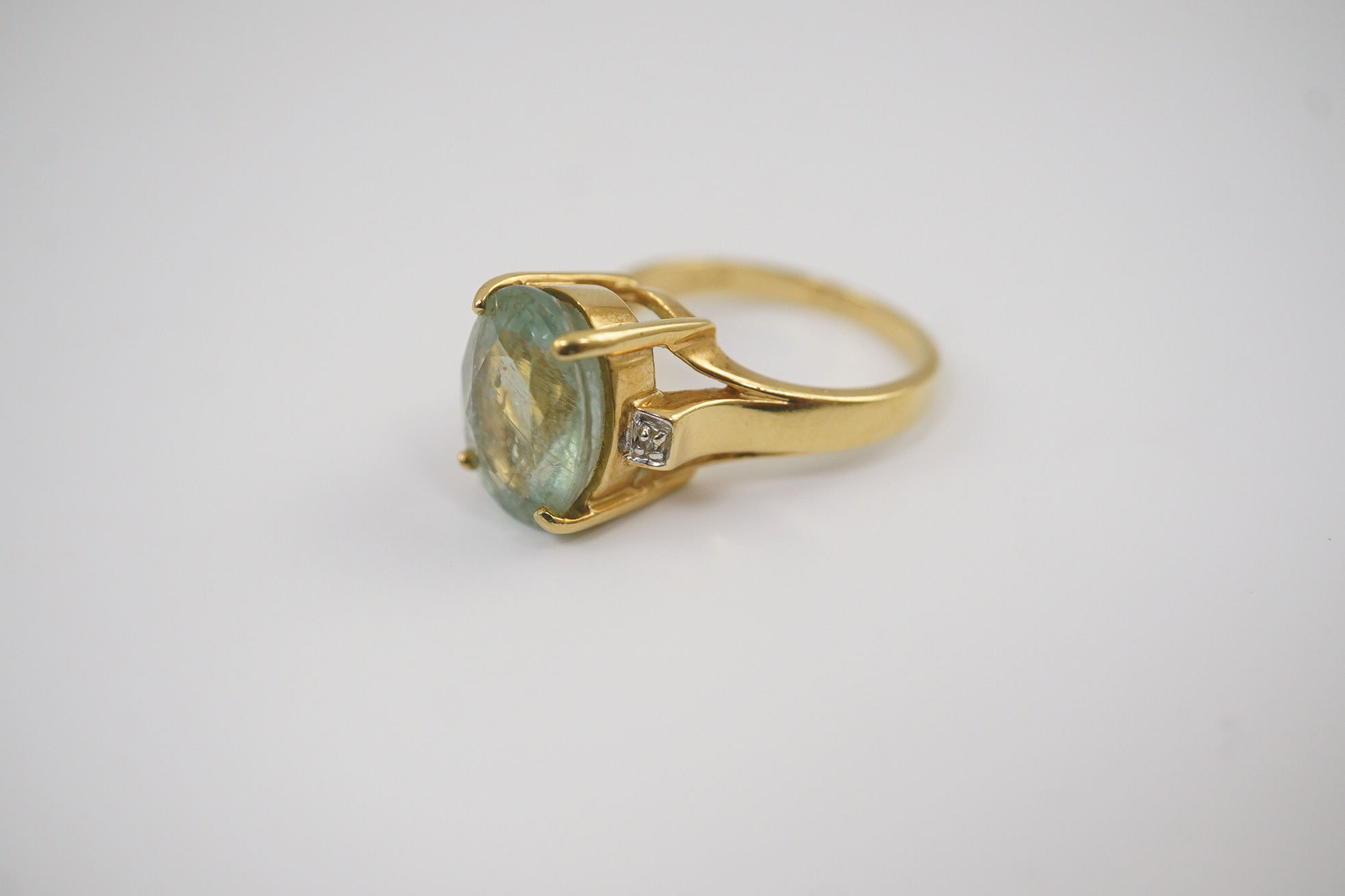 A modern 18ct gold and oval cut pale green tourmaline set dress ring, with two stone diamond chip set shoulders